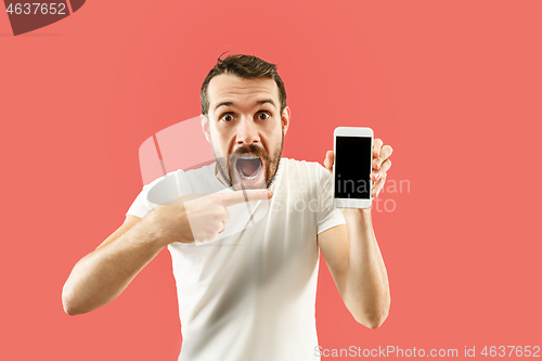 Image of Young handsome man showing smartphone screen isolated on coral background in shock with a surprise face