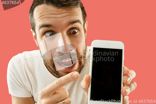 Image of Young handsome man showing smartphone screen isolated on coral background in shock with a surprise face