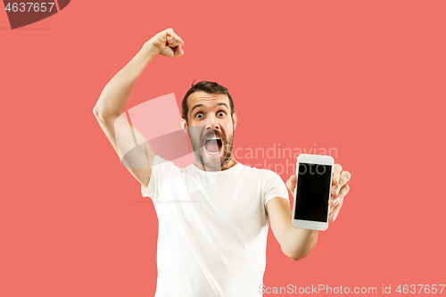 Image of Young handsome man showing smartphone screen isolated on coral background in shock with a surprise face