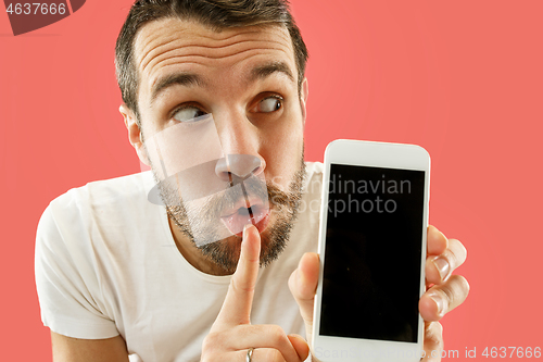 Image of Young handsome man showing smartphone screen isolated on coral background in shock with a surprise face