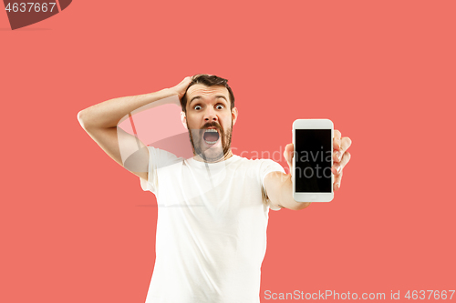 Image of Young handsome man showing smartphone screen isolated on coral background in shock with a surprise face