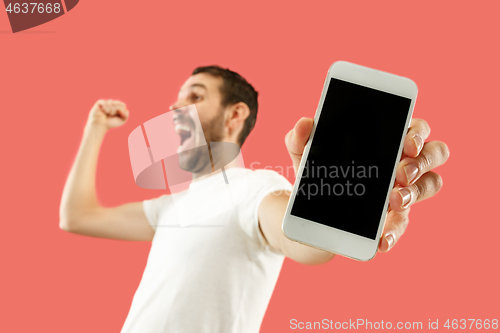 Image of Young handsome man showing smartphone screen isolated on coral background in shock with a surprise face