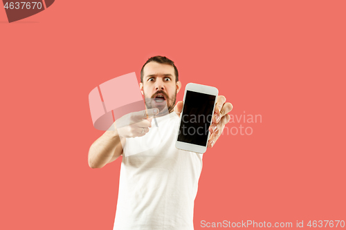 Image of Young handsome man showing smartphone screen isolated on coral background in shock with a surprise face