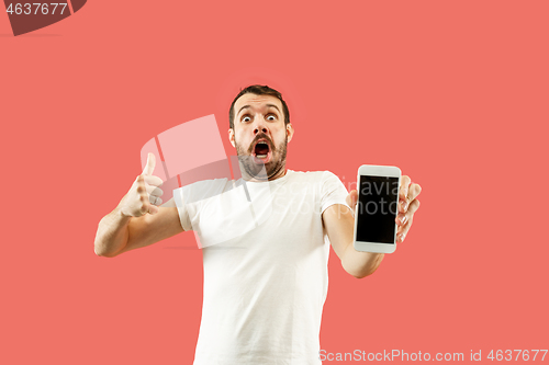 Image of Young handsome man showing smartphone screen isolated on coral background in shock with a surprise face