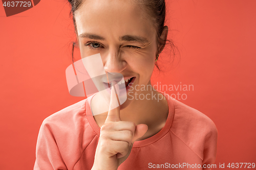 Image of The young woman whispering a secret behind her hand over coral background