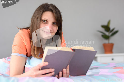 Image of The girl reads a book and looked into the frame with a smile