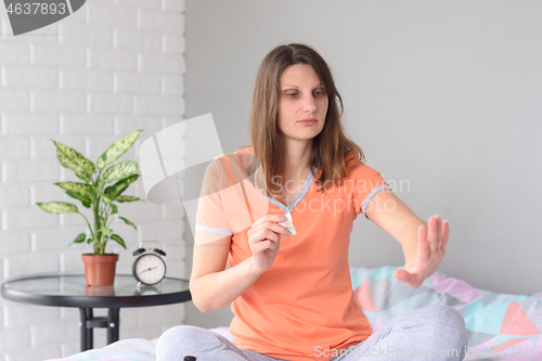 Image of The girl in pajamas on the day off sitting on the bed looks at her nails after removing the varnish