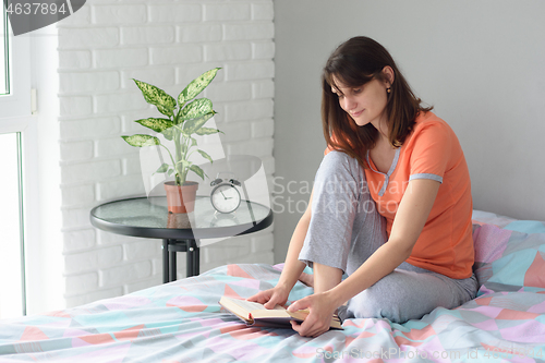 Image of Girl sitting in bed in pajamas and reading a book