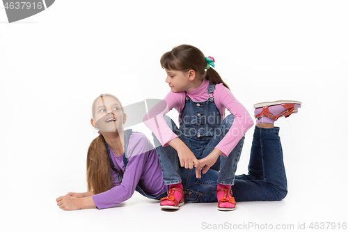 Image of Two sisters play against a white background in denim jumpsuits