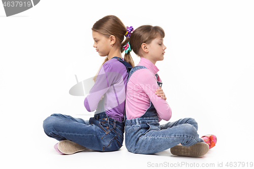 Image of Two quarrelled girls sit with their backs to each other on a white background