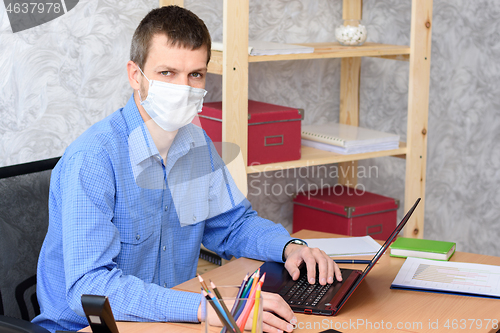 Image of Portrait of an office worker in a medical mask at a desk