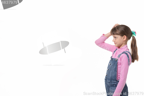 Image of The girl puzzled scratches her head and looks at an empty spot in the frame.