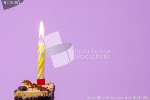 Image of Festive burning candle on a cake on a light purple background