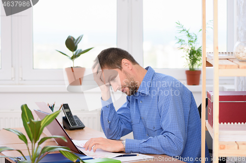 Image of Upset office worker looking at documents clutching his head