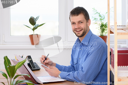 Image of Young successful businessman writes in a notebook and looked into the frame