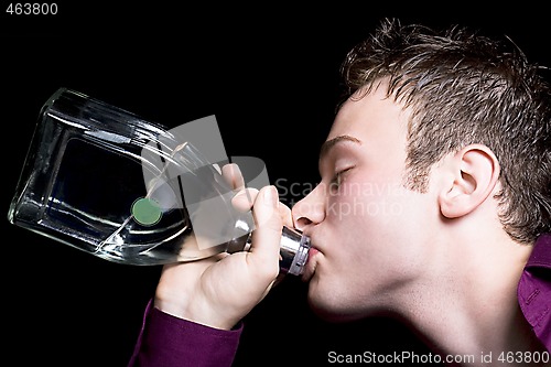 Image of The young man drinks vodka from a bottle. Isolated on black