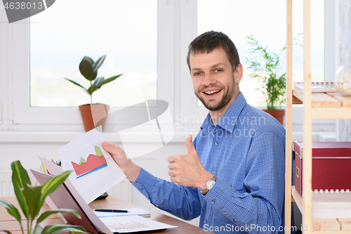 Image of Young businessman shows charts and thumb up