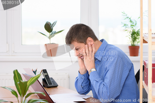 Image of Office clerk grimacing grimacing pain on his face looking at a laptop