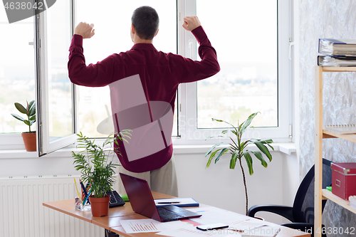 Image of Office worker does gymnastics standing by the window