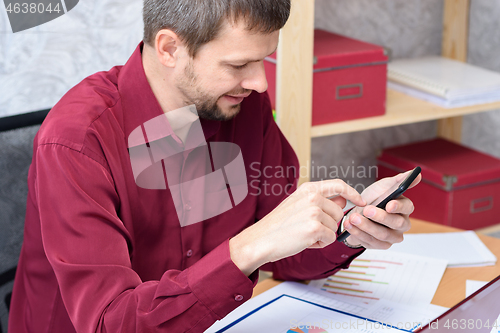 Image of man with a smile looks at the smartphone at the desk in the office