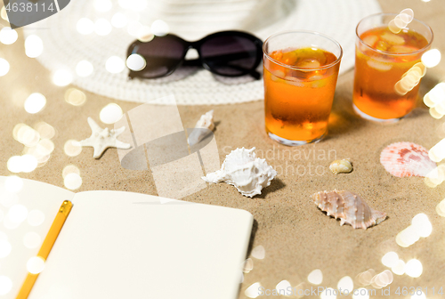 Image of notebook, cocktails, hat and shades on beach sand