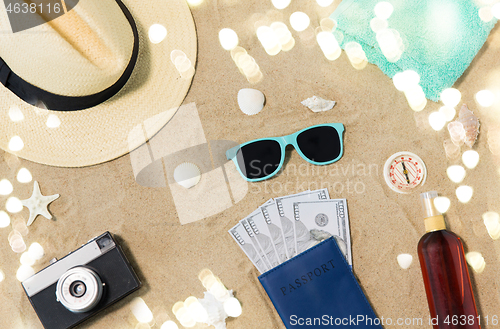 Image of money in passport, shades and hat on beach sand