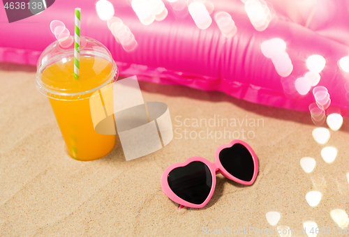 Image of sunglasses, juice and pool mattress on beach sand