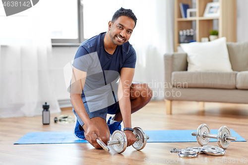 Image of smiling indian man assembling dumbbells at home