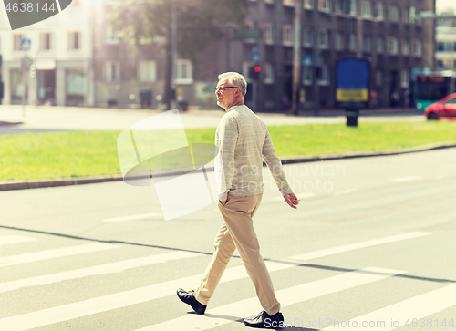 Image of senior man walking along city crosswalk