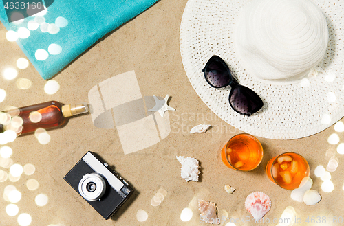 Image of drinks, hat, camera and sunglasses on beach sand