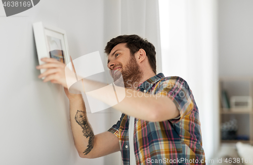 Image of man hanging picture in frame to wall at home