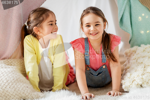 Image of happy girls lying in kids tent at home