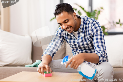 Image of indian man cleaning table with detergent at home