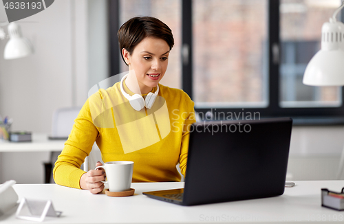 Image of businesswoman with laptop drinks coffee at office