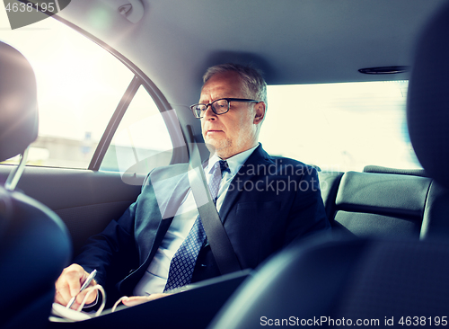 Image of senior businessman with papers driving in car