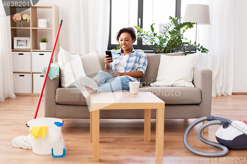 Image of woman with smartphone resting after home cleaning