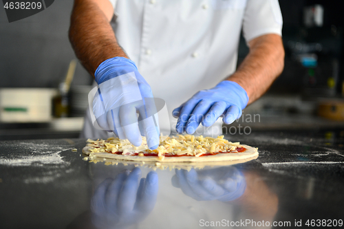 Image of chef  with protective coronavirus face mask preparing pizza