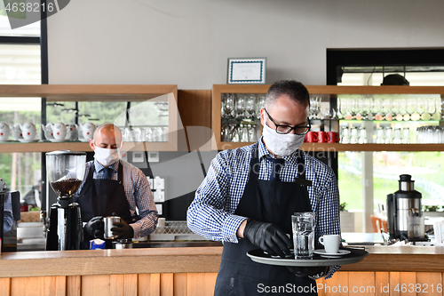 Image of waiter in a medical protective mask serves  the coffee in restau
