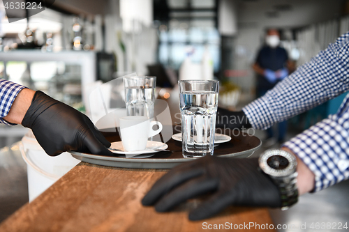 Image of waiter in a medical protective mask serves  the coffee in restau