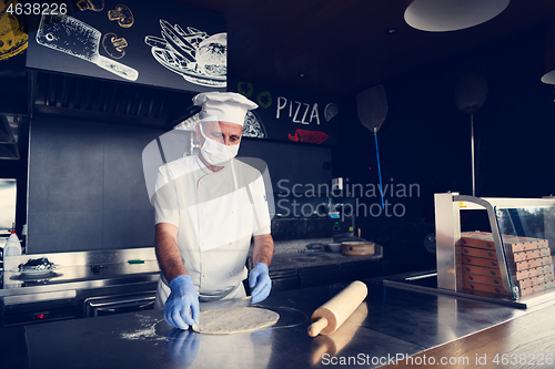 Image of chef  with protective coronavirus face mask preparing pizza