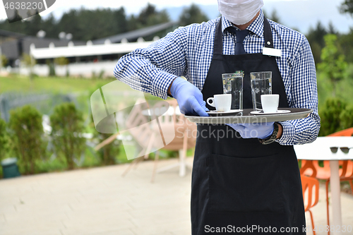 Image of waiter in a medical protective mask serves  the coffee in restau