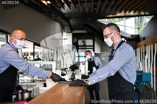 Image of waiter in a medical protective mask serves  the coffee in restau