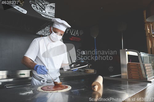 Image of chef  with protective coronavirus face mask preparing pizza