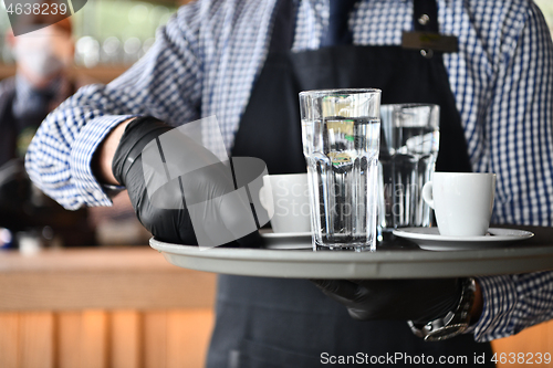 Image of waiter in a medical protective mask serves  the coffee in restau