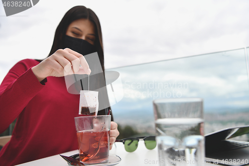 Image of woman in restaurant drinking tea wearingmedical  face mask