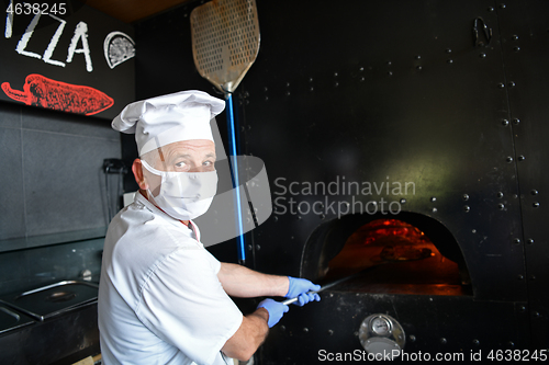 Image of chef  with protective coronavirus face mask preparing pizza