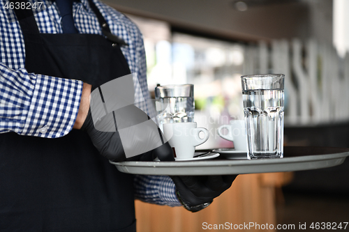 Image of waiter in a medical protective mask serves  the coffee in restau