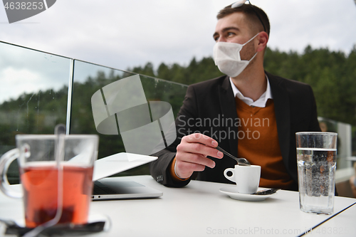 Image of man in restaurant drinking coffee wearing face mask