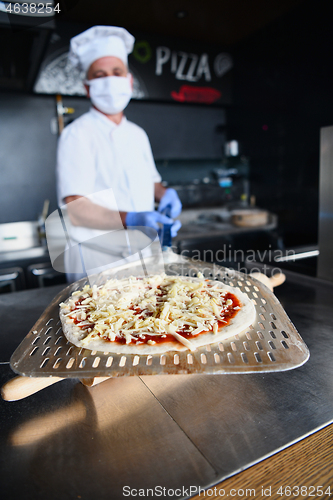 Image of chef  with protective coronavirus face mask preparing pizza