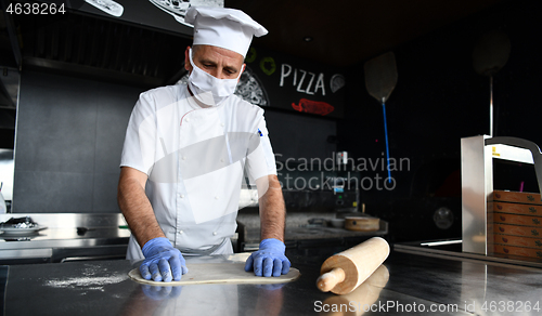 Image of chef  with protective coronavirus face mask preparing pizza